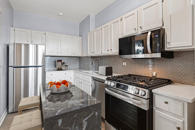 kitchen featuring white cabinets, tasteful backsplash, light stone counters, a sink, and appliances with stainless steel finishes