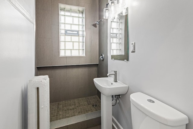 bathroom featuring a sink, radiator, a tile shower, and toilet