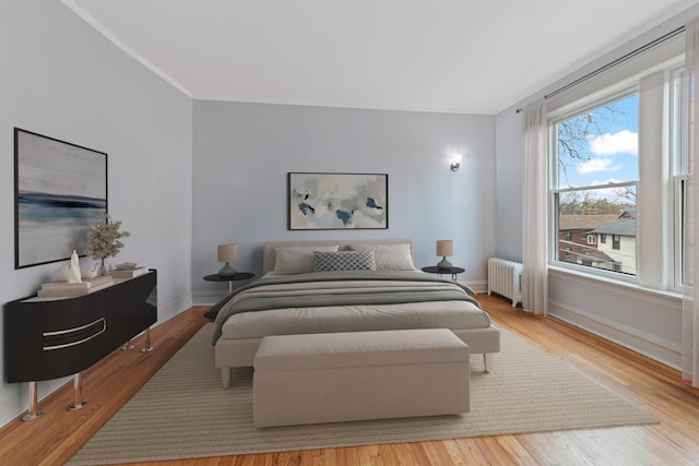 bedroom with radiator, baseboards, ornamental molding, and wood finished floors