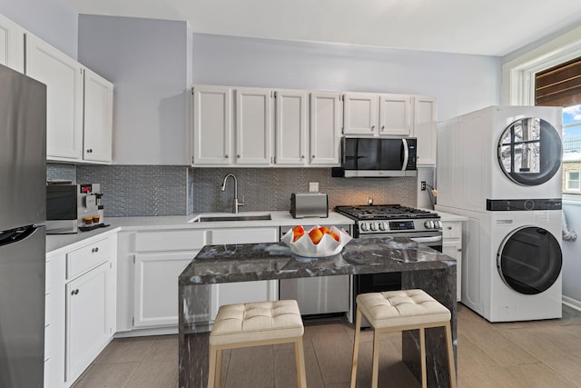 kitchen featuring stacked washer and dryer, white cabinets, a sink, backsplash, and stainless steel appliances