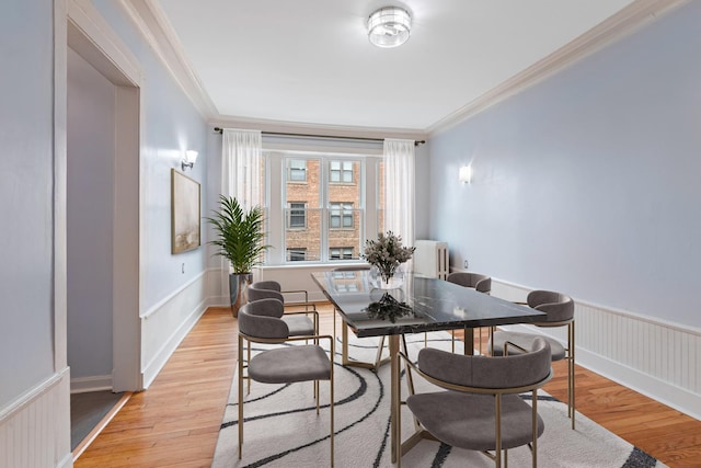 dining area featuring crown molding, a wainscoted wall, radiator, and light wood-style floors
