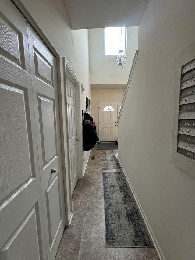 hall with baseboards, dark colored carpet, built in shelves, and a towering ceiling