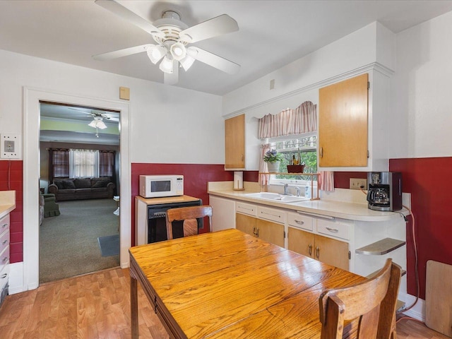 kitchen featuring ceiling fan, a sink, light countertops, white microwave, and light wood-style floors