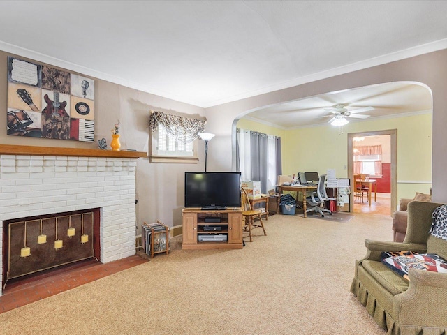 carpeted living area featuring arched walkways, ornamental molding, a fireplace, and ceiling fan