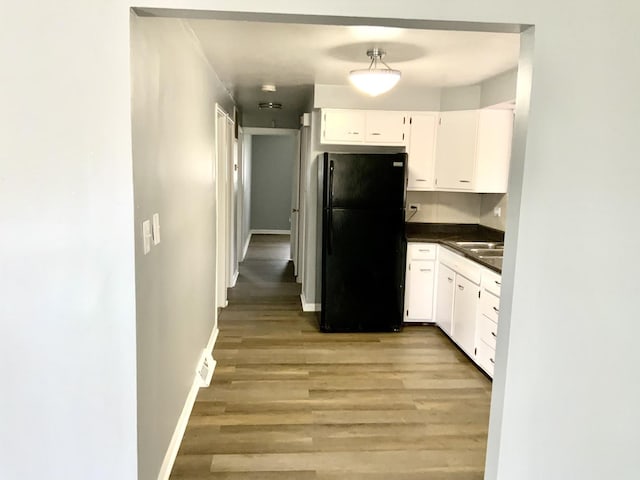 kitchen with dark countertops, baseboards, freestanding refrigerator, light wood finished floors, and white cabinetry