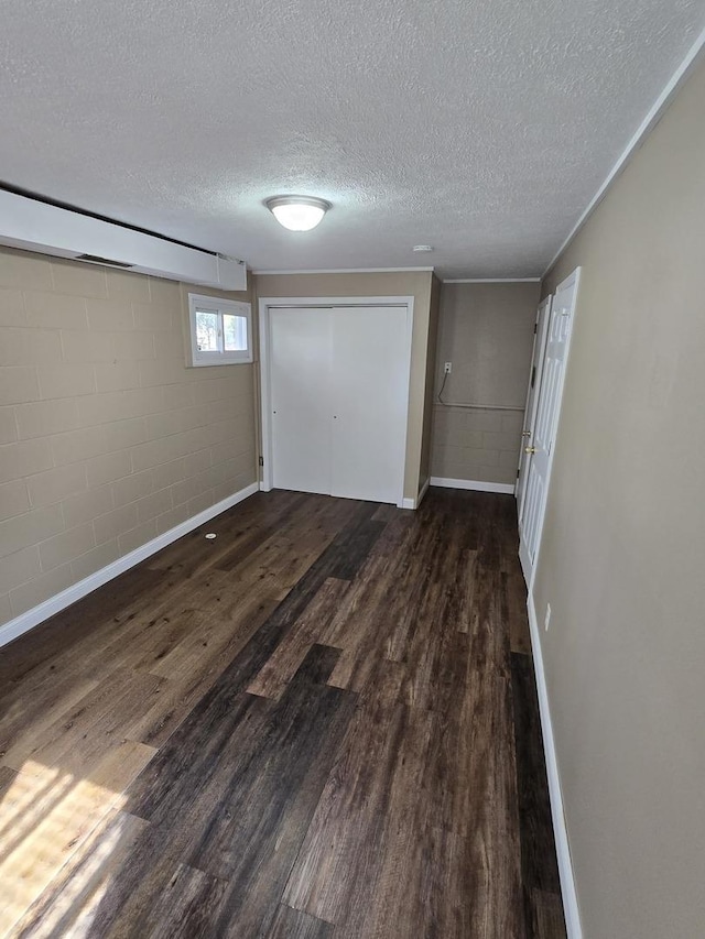unfurnished bedroom with a closet, baseboards, dark wood-style floors, a textured ceiling, and concrete block wall