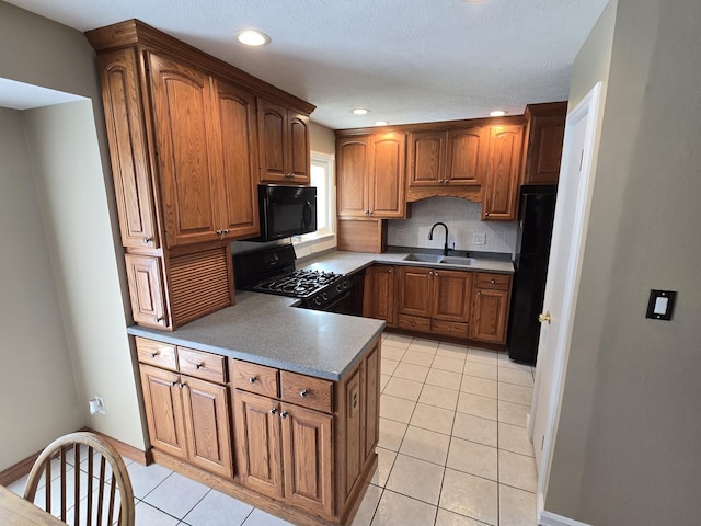 kitchen featuring a sink, brown cabinetry, a peninsula, light tile patterned floors, and black appliances
