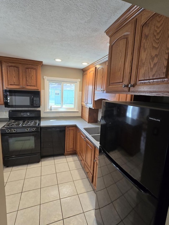 kitchen with light tile patterned floors, black appliances, brown cabinets, and a textured ceiling