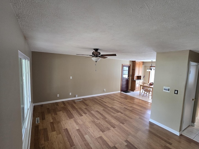 unfurnished living room with a textured ceiling, ceiling fan with notable chandelier, baseboards, light wood-type flooring, and visible vents