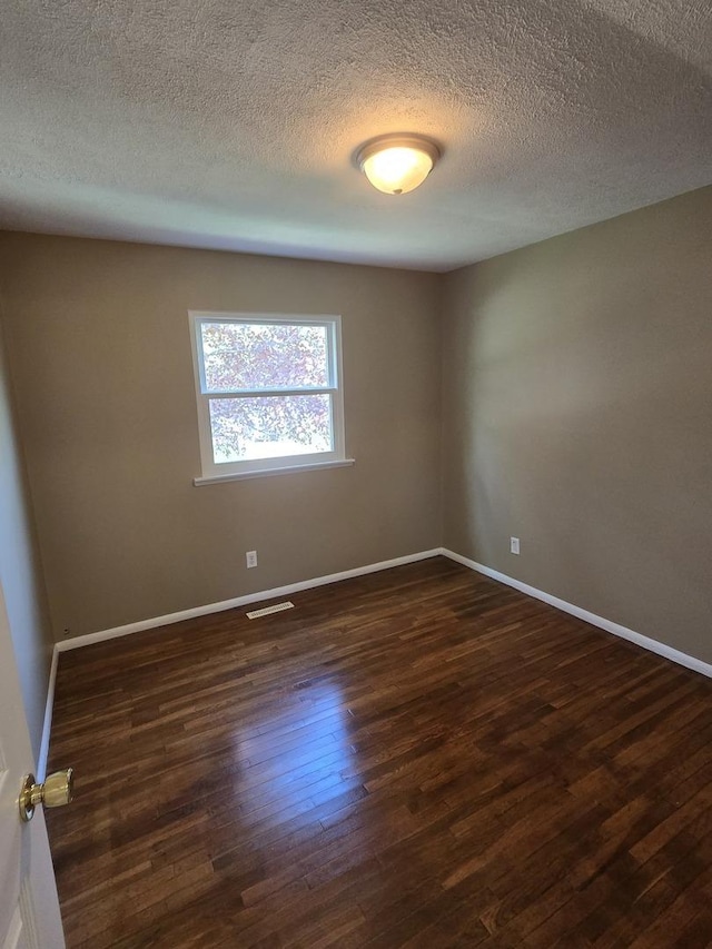 unfurnished room with a textured ceiling, dark wood finished floors, and baseboards
