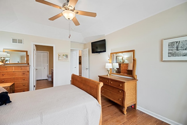 bedroom featuring a ceiling fan, visible vents, vaulted ceiling, wood finished floors, and baseboards