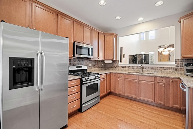 kitchen featuring light wood-style floors, light stone counters, a sink, backsplash, and stainless steel appliances
