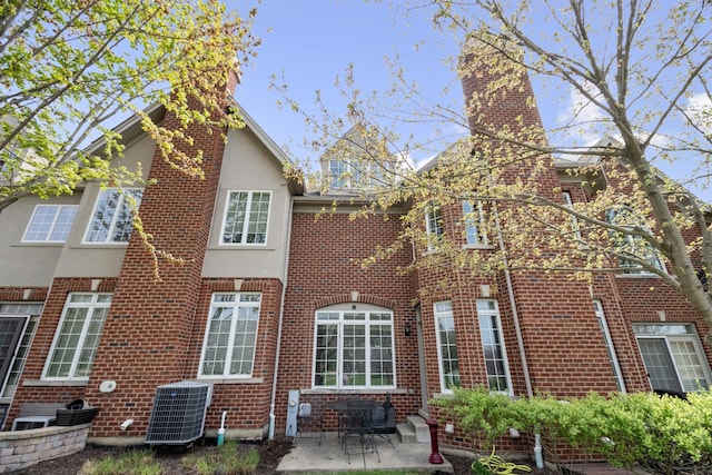 back of house with central air condition unit, a patio, a chimney, and brick siding
