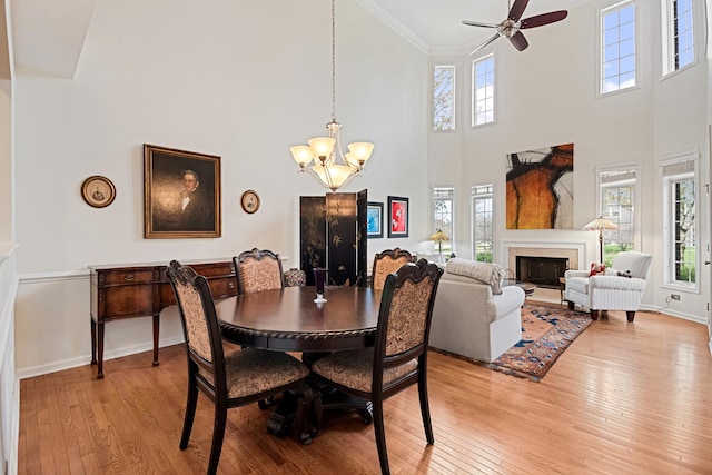 dining area with crown molding, ceiling fan with notable chandelier, a high ceiling, and light wood-type flooring