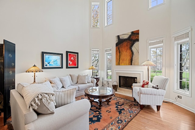 living area with a towering ceiling, wood finished floors, a healthy amount of sunlight, and a fireplace