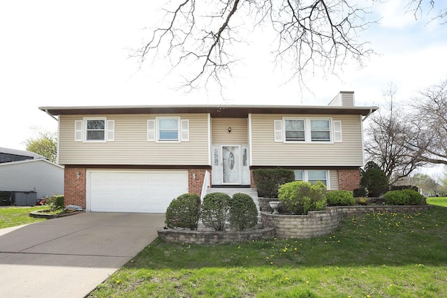 bi-level home with brick siding, an attached garage, driveway, and a chimney