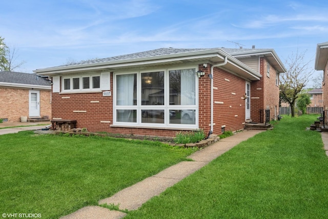back of house featuring a lawn, brick siding, and roof with shingles