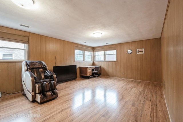 living area featuring light wood-type flooring, wood walls, and visible vents