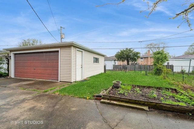 detached garage featuring fence and a garden