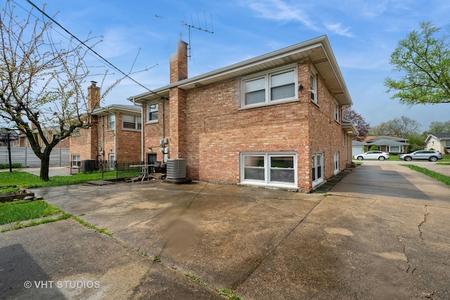 back of house with fence, central air condition unit, a chimney, and brick siding