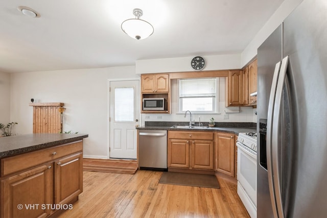 kitchen with dark countertops, a sink, baseboards, light wood-style floors, and stainless steel appliances