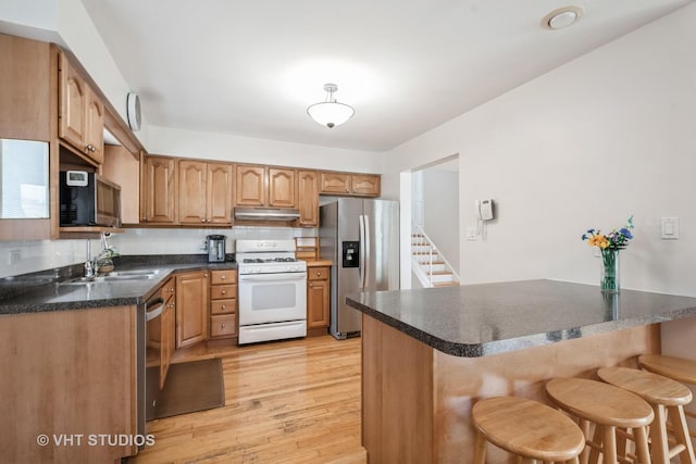 kitchen featuring a sink, a breakfast bar area, stainless steel appliances, a peninsula, and under cabinet range hood