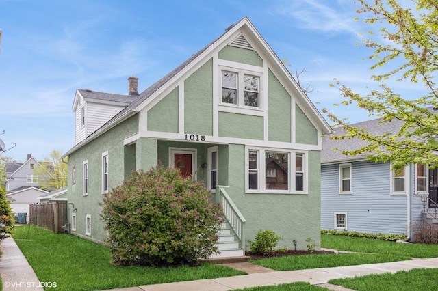 tudor-style house featuring a chimney, roof with shingles, stucco siding, and a front yard
