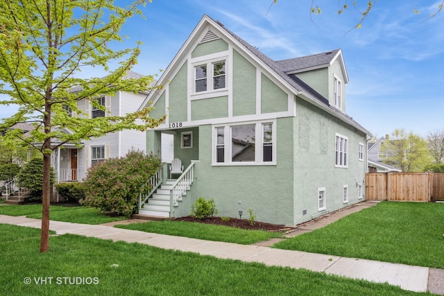 tudor-style house with fence, a front yard, and stucco siding