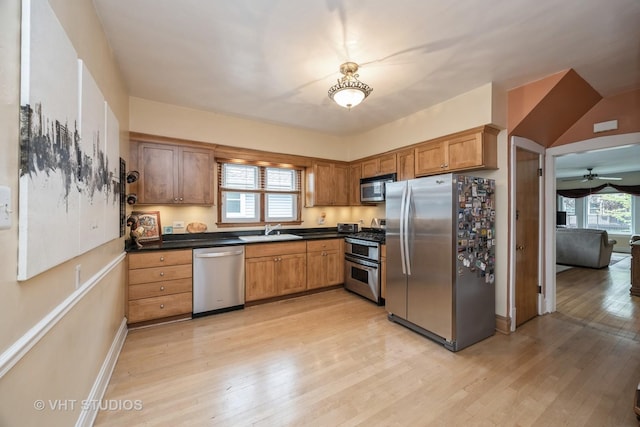 kitchen featuring dark countertops, appliances with stainless steel finishes, light wood-style floors, and a sink
