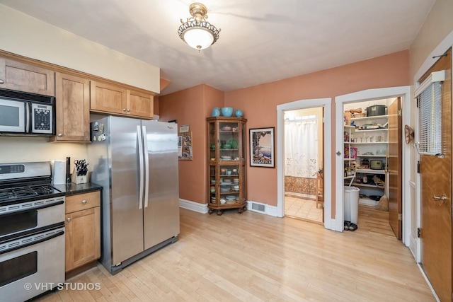 kitchen with brown cabinets, dark countertops, appliances with stainless steel finishes, light wood-style floors, and baseboards