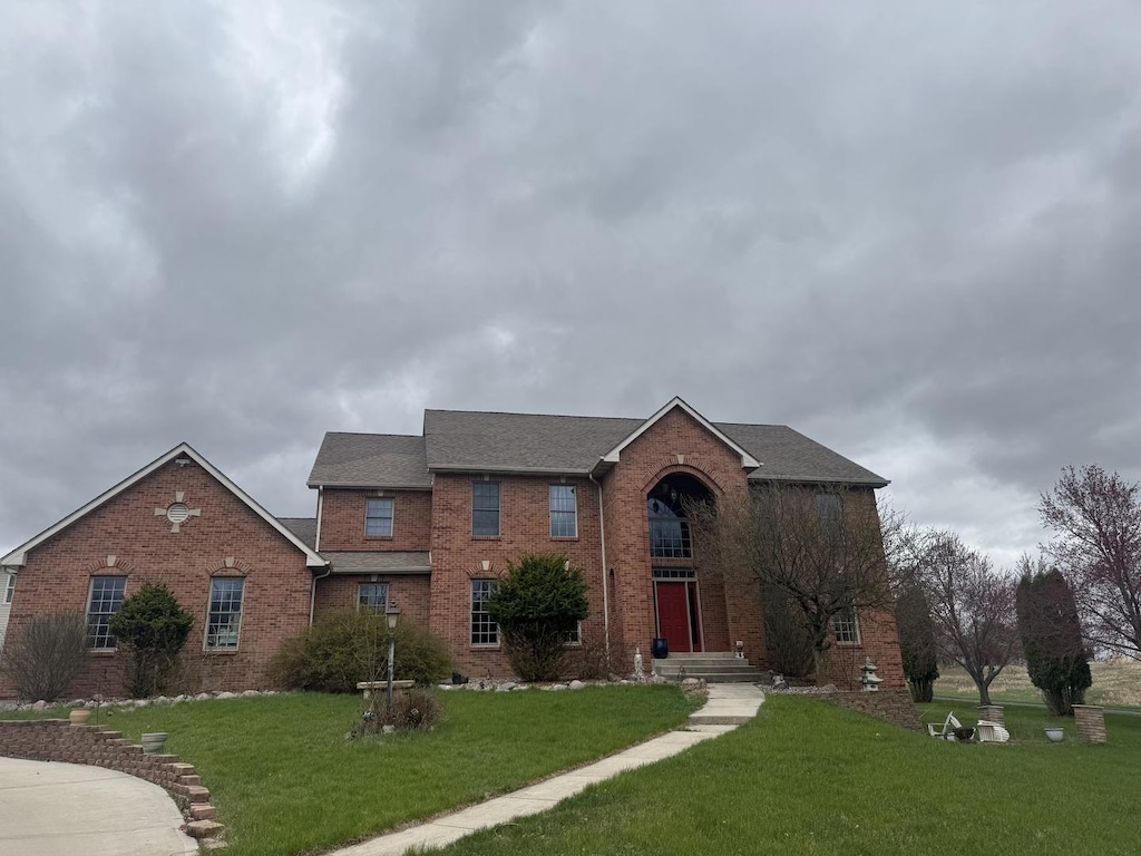 traditional-style home with a shingled roof, a front lawn, and brick siding