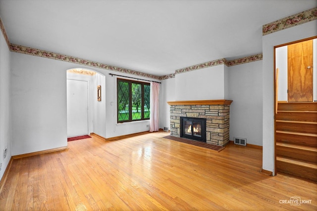 33 Chestnut Ave, Clarendon Hills, IL 60514 - unfurnished living room featuring light wood-style flooring, a stone fireplace, baseboards, arched walkways, and stairway