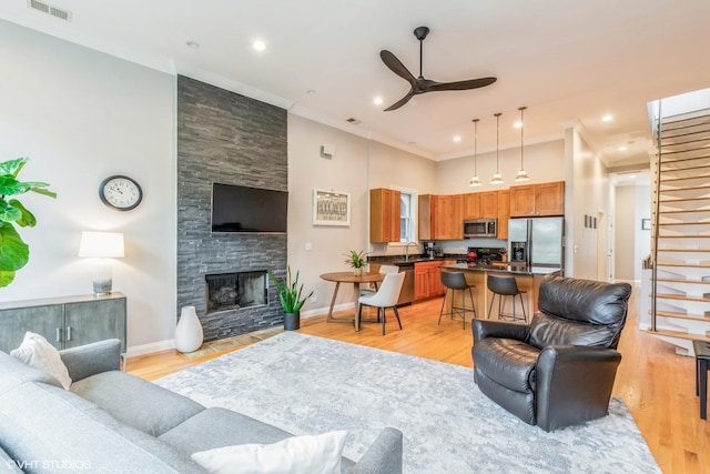 living area featuring a ceiling fan, a fireplace, crown molding, visible vents, and baseboards