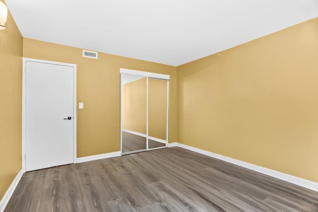 unfurnished bedroom featuring baseboards, visible vents, dark wood-style floors, and a closet