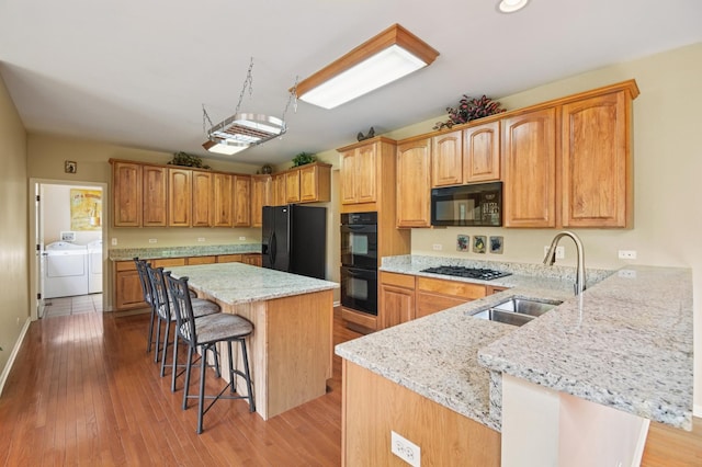 7770 Farrell Dr, Lakewood, IL 60014 - kitchen featuring black appliances, separate washer and dryer, a kitchen breakfast bar, light wood-style flooring, and light stone counters
