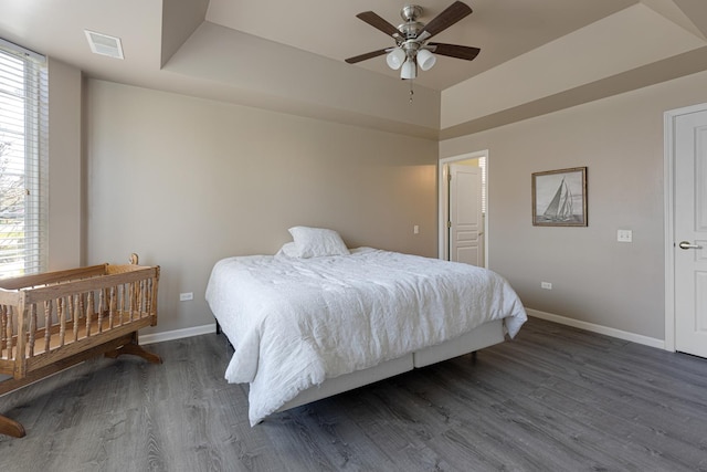 bedroom featuring baseboards, dark wood-style floors, a tray ceiling, and a ceiling fan