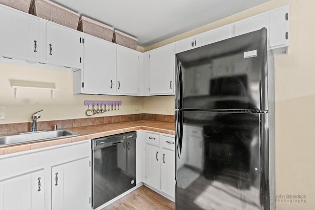 kitchen with white cabinetry, a sink, black appliances, and light wood-style floors