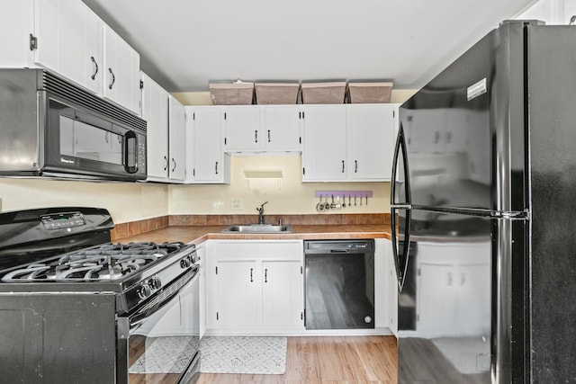 kitchen featuring a sink, light wood finished floors, black appliances, and white cabinets