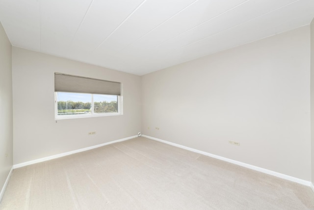 spare room featuring light colored carpet and baseboards