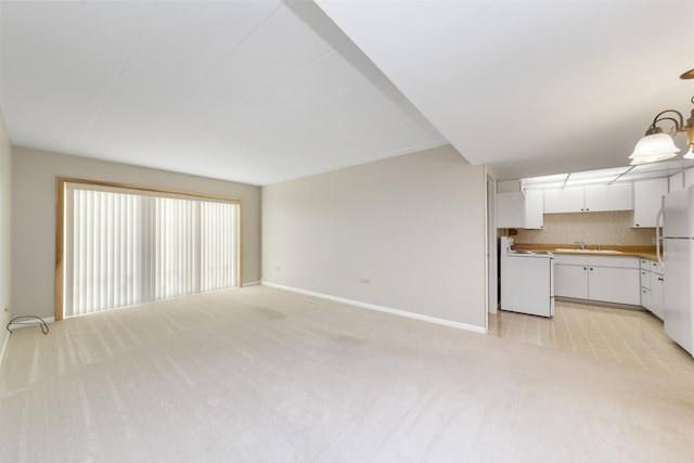 unfurnished living room with light colored carpet, a sink, and baseboards