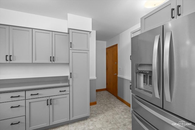 kitchen featuring stainless steel fridge with ice dispenser, light floors, gray cabinets, and baseboards