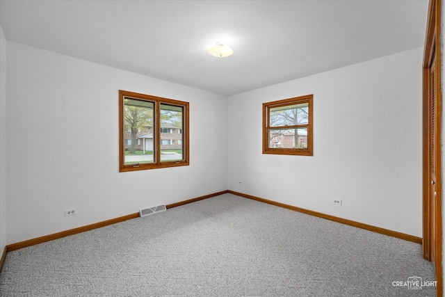 spare room featuring carpet flooring, baseboards, plenty of natural light, and visible vents