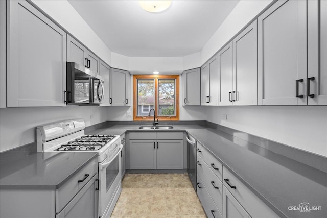 kitchen with dark countertops, appliances with stainless steel finishes, a sink, and gray cabinets