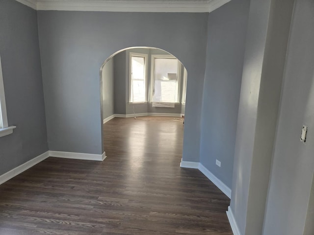 spare room featuring crown molding, arched walkways, dark wood finished floors, and baseboards