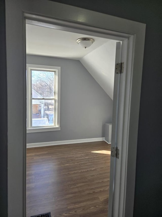 additional living space with baseboards, vaulted ceiling, wood finished floors, and visible vents