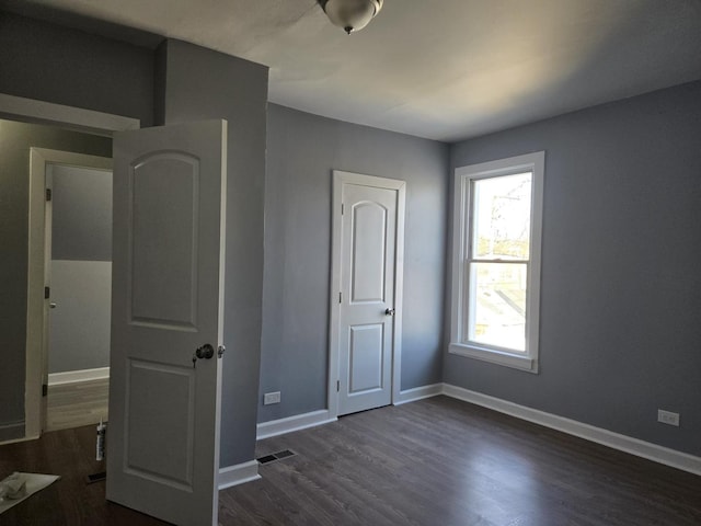 unfurnished bedroom with baseboards, dark wood-type flooring, and visible vents