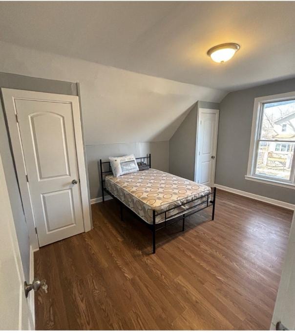 bedroom with baseboards, vaulted ceiling, and wood finished floors