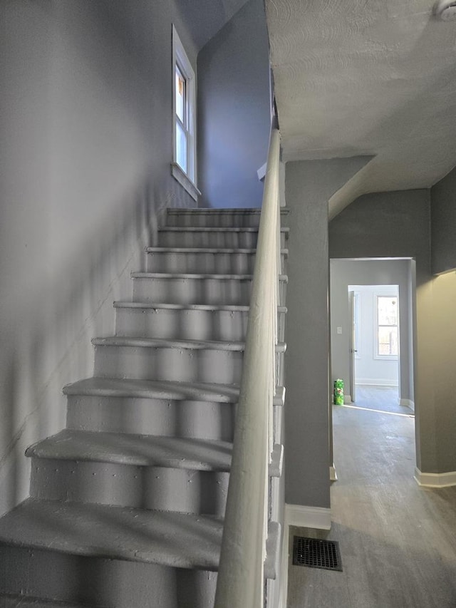staircase featuring a textured ceiling, baseboards, visible vents, and plenty of natural light