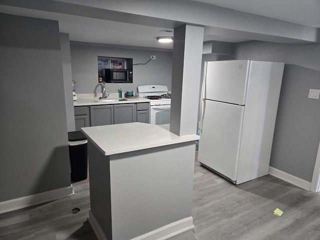 kitchen with light wood-type flooring, a sink, gray cabinetry, and white appliances