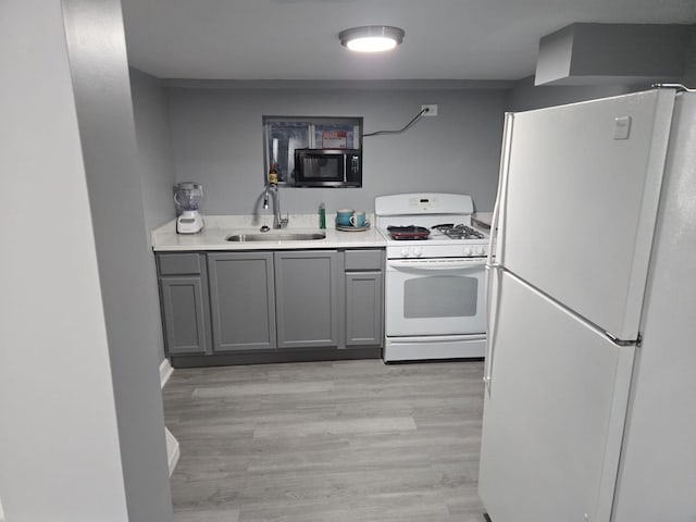 kitchen featuring white appliances, light wood-type flooring, light countertops, a sink, and gray cabinetry